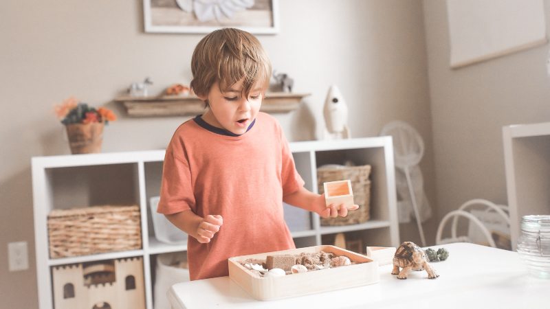 boy orange shirt playing with sandbox in kids room